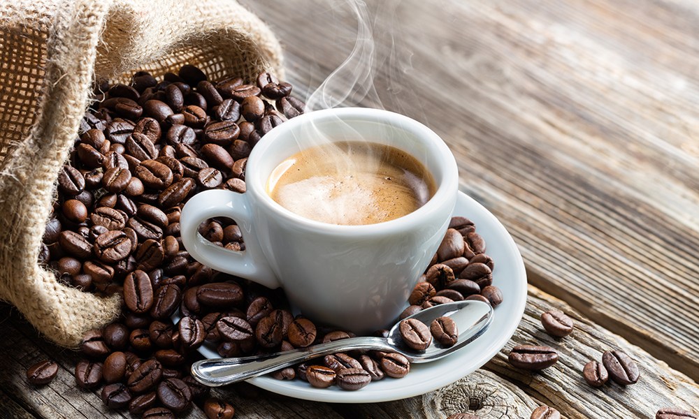 A warm cup of coffee and spoon on a saucer with coffee beans